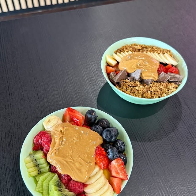 Two açaí bowls topped with peanut butter, fruit, and granola