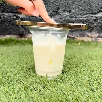 An iced drink in a clear cup on the grass, a hand setting a gold lid on top