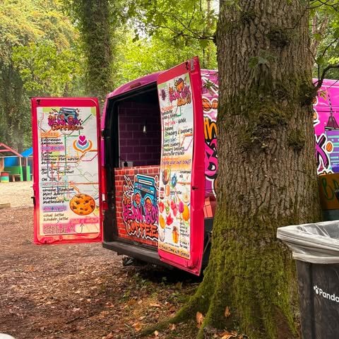 The pink Bean Box coffee trailer open for service under the trees at an outdoor event, menu boards up